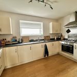 Modern kitchen with light cabinets and wooden floor.