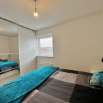 Modern bedroom with teal accents and mirrored wardrobe.