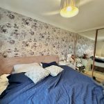 Cosy bedroom with floral wallpaper and mirrored wardrobe.