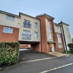 Red-brick apartment building with balconies and driveway.