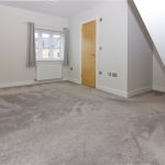 Minimalist grey carpeted room with wooden door.