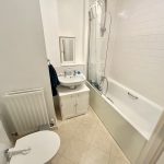 Compact white tiled bathroom with bathtub and sink.