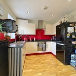 Modern kitchen with red accents and wooden flooring.