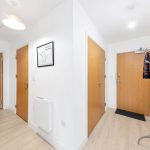 Modern flat hallway with wooden doors and coat rack.