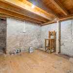 Empty basement with exposed wooden beams, brick walls.