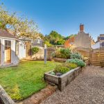 Sunny garden with wooden shed and flower beds.