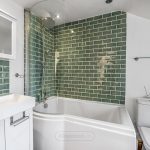 Modern bathroom with green tiled walls and white fixtures.
