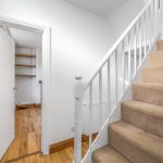 Carpeted staircase and open doorway in bright hallway.