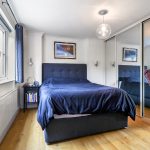 Modern bedroom with mirrored wardrobe and dark furnishings.