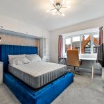 Modern bedroom with blue bed and desk area.