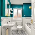 Modern teal bathroom with sink, toilet, and bath.