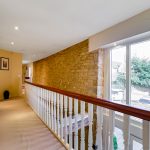 Stone-walled hallway with large windows and railing.