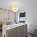 Modern bedroom with beige decor and feather chandelier.