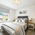 Elegant modern bedroom with chandelier and decorative pillows.