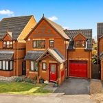 Brick house with red door and large driveway.