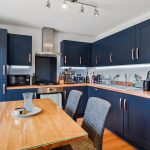 Modern kitchen with navy cabinets and wooden table.