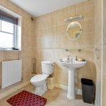 Tiled bathroom with toilet, sink, and window.
