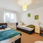 Bright twin bedroom with playful decor and fan.