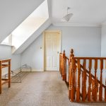 Attic landing with wooden railing and small window.