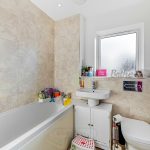 Modern bathroom with beige tiles and bathtub.
