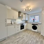 Modern white kitchen with appliances and wooden floor.