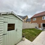 Garden with shed and modern houses in background.
