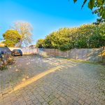 Spacious driveway with car, trees, and brick building.