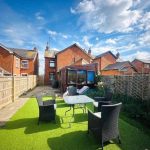 Sunny garden with patio furniture and green lawn.