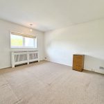 Spacious empty room with window and chest of drawers.